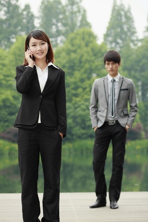 Businesswoman talking on the phone, businessman standing in the backgroundの写真素材
