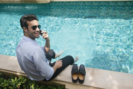 Businessman talking on the phone with feet in swimming poolの写真素材