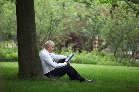 Businessman reading book under a treeの写真素材