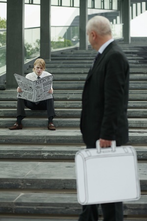 Businessman reading newspaper on the stairs, another businessman carrying briefcaseの写真素材