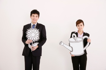 Businessman holding flower while businesswoman is holding a watering canの写真素材