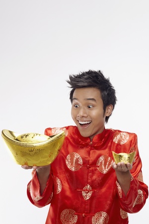 Man holding a big and small gold ingot with outstretched arms の写真素材