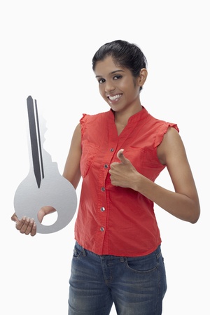 Excited woman holding a big key and showing thumbs upの写真素材