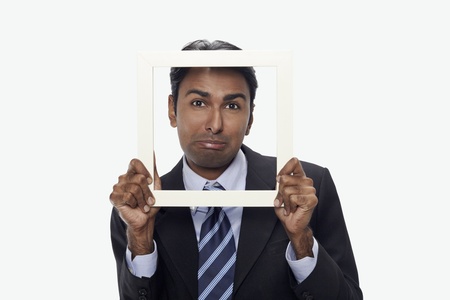 Businessman sulking and looking through cutout paper frame