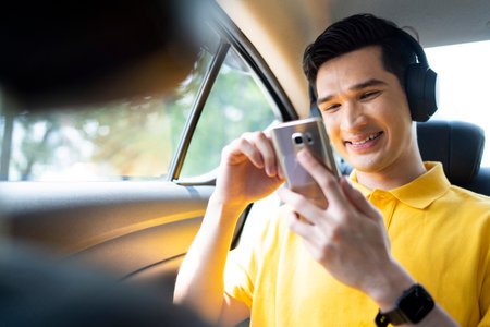 Young Asian man smiling and using a mobile phone in car