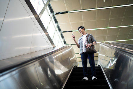 Young Asian man using his mobile phone while standing on escalator