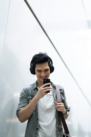Young Asian man smiling at his phone while wearing headphonesの写真素材