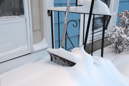 shovel buried by snow outside front door after blizzardの写真素材