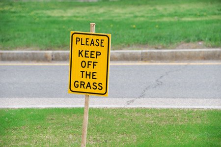 please keep off grass warning sign on the meadow along urban streetの写真素材