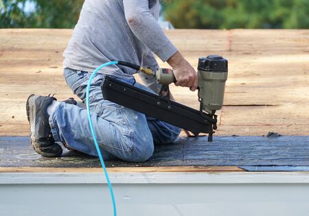 handyman using nail gun to install shingle to repair roofの写真素材