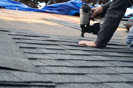 handyman using nail gun to install shingle to repair roofの写真素材