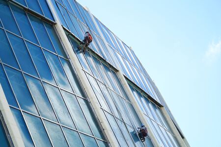 manual workers hanging outside office building cleaning glass wallの写真素材