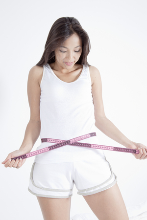Young woman measuring waist with tapeの写真素材