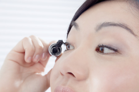 Young woman putting on mascaraの写真素材