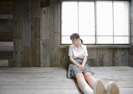Girl sitting by window in school uniformの写真素材