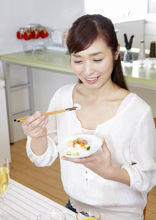 Young woman eating chirashi sushiの写真素材