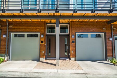 Gragage and entrance doors of brand new townhouses with wood finished wall on sunny day in British Columbia