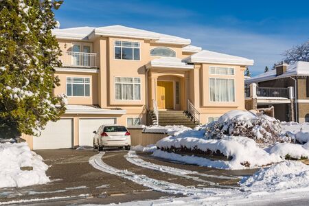 Luxury residential house with front yard in snow and car on the driveway. North American family house on winter sunny dayの写真素材