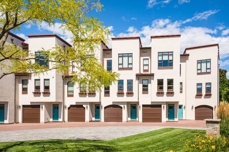 Residential townhouses with decorative acacia tree in front on blue sky background