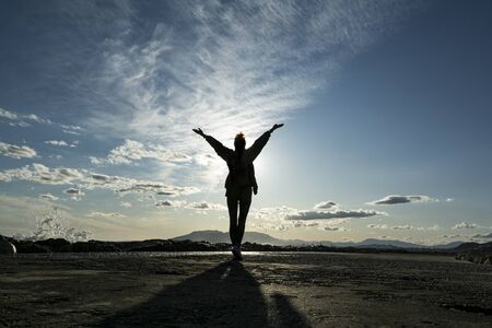 Free happy woman raising arms watching the sun in the background at blue sunset.の写真素材