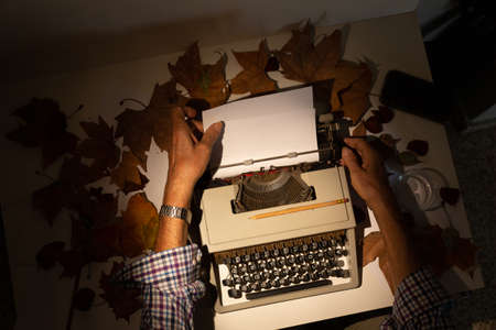 Top view of mans hands on a typewriter with autumn leavesの写真素材
