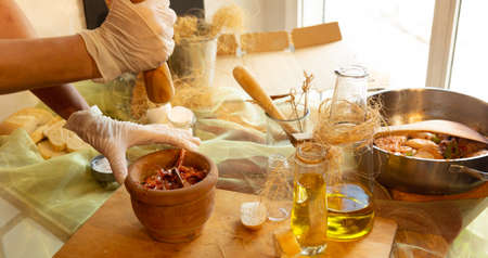 Womans hands with gloves cooking squid in sauce, pounding prawn heads in mortarの写真素材