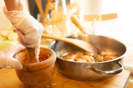 Womans hands with gloves cooking squid in sauce, pounding prawn heads in mortar