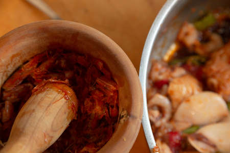 Womans hands with gloves cooking squid in sauce, mashing prawn headsの写真素材