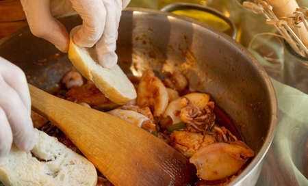Womans hands with gloves cooking squid in sauce, mashing prawn headsの写真素材