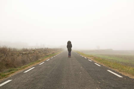 Unrecognisable woman, walking on a cold and foggy mountain roadの写真素材