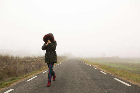 Unrecognisable woman, walking on a cold and foggy mountain roadの写真素材