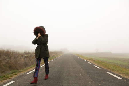 Unrecognisable woman, walking on a cold and foggy mountain roadの写真素材
