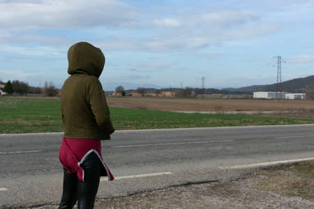 Woman with hood, hands in pockets waiting on the road. unrecognizableの写真素材