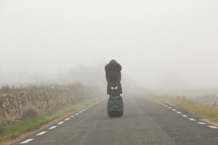 Woman dragging a suitcase along the road on a foggy dayの写真素材