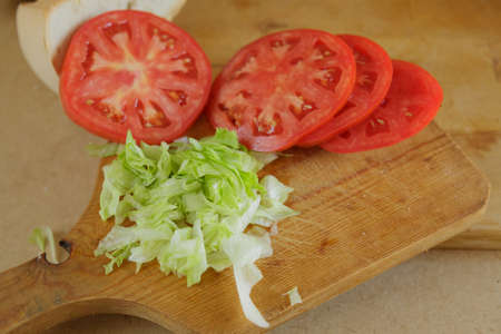 Hamburger preparation with tomato and lettuce on wooden boardの写真素材