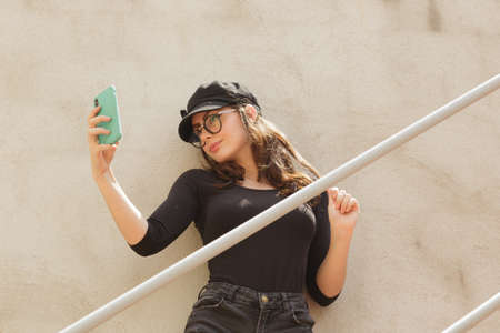 Cool woman taking self portrait on cellphone on stairs
