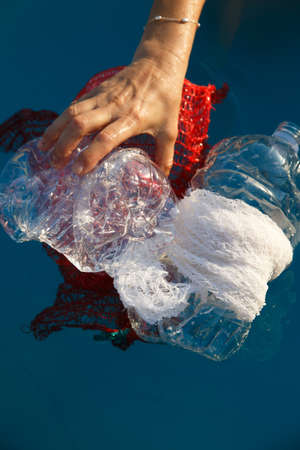Womans hands picking up and plastic bottles with net bags floating in the water, plastic...