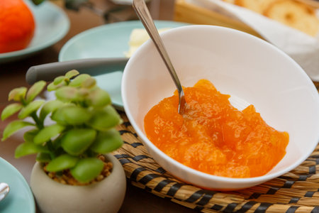 A White Bowl of Fruit Jam sitting next to a Green Plant in a Breakfast table arrangementの写真素材