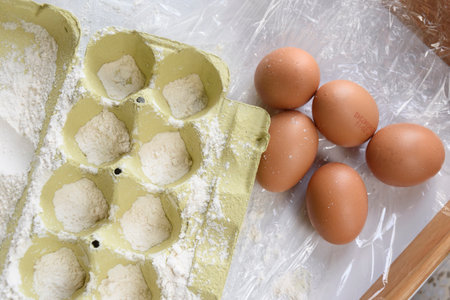 A dozen eggs are resting on a kitchen table conveniently positioned alongside a carton filled with...
