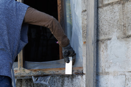 A dedicated worker uses a putty knife to restore an old window frame, showcasing fine craftsmanshipの写真素材