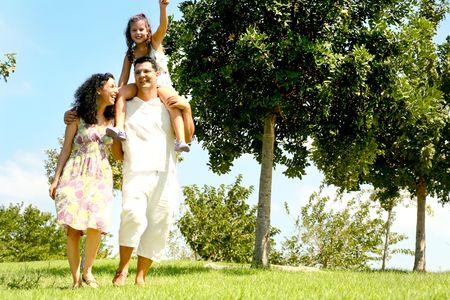 Dad carrying daughter on his shoulders while crossing garden with his wifeの写真素材