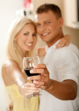 Smiling young couple sharing wine glass in kitchen and facing cameraの写真素材