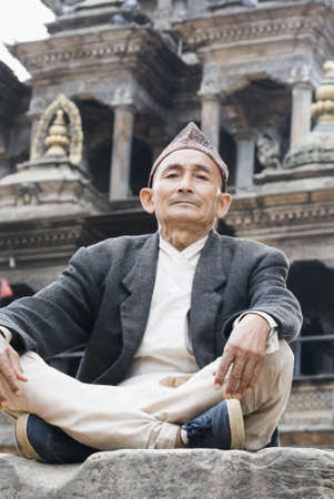Low angle view of a senior man sitting cross-legged on a rockの写真素材