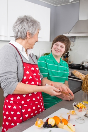 Grandmother teaching young boy to cook meat - family life at home in the kitchenの写真素材