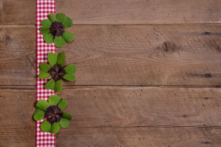 Wooden background with red and white checkered ribbon and green cloversの写真素材