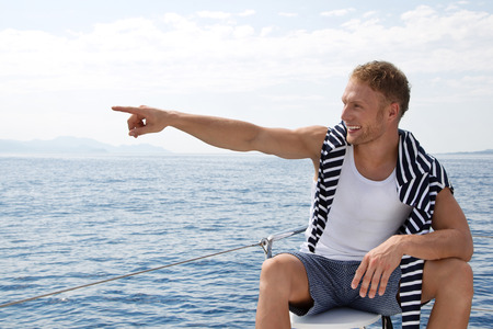 Young man on a sailing boat pointing at something.