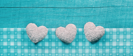 Turquoise wooden shabby chic background with white hearts on a checked fabric frame.