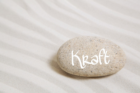 Stone in the sand with the german word power. Idea background for spa and mental therapy.の写真素材