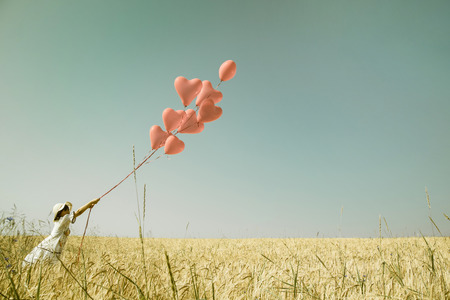 Young romantic girl in summertimes with red heart balloons walking in a field of wheat.の写真素材