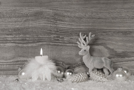 Grey, white silver christmas decoration with one burning candle on wooden background with reindeer.の写真素材